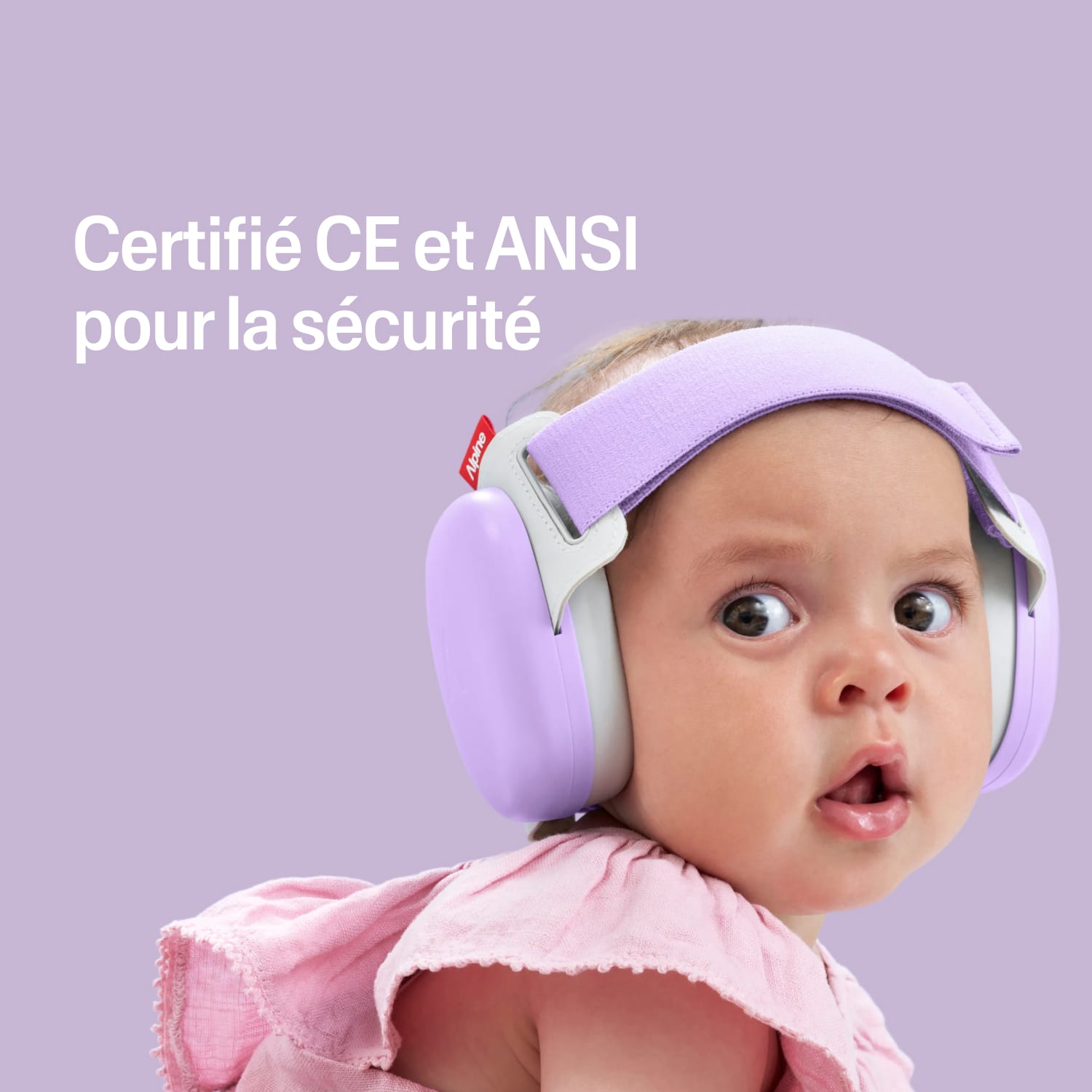 Baby wearing a purple muffy baby with certification text on a pink heart-patterned background