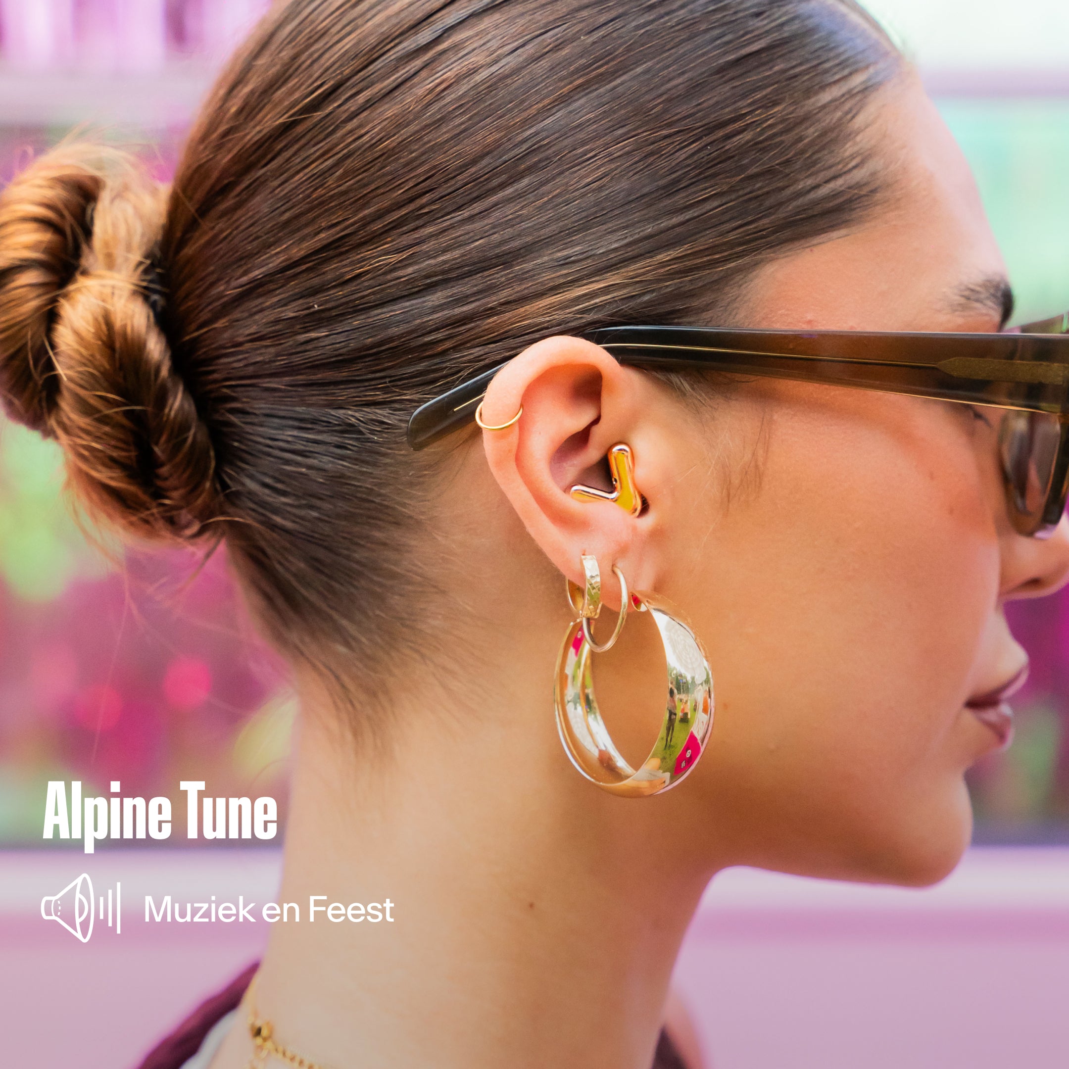 Alpine Tune gouden oordopje gedragen door een vrouw met zonnebril en oorringen, met de tekst &