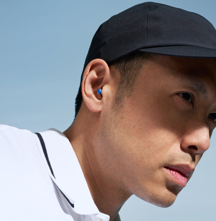 Alpine 24h Le Mans® earplug worn in the ear by a man in a black cap and white shirt