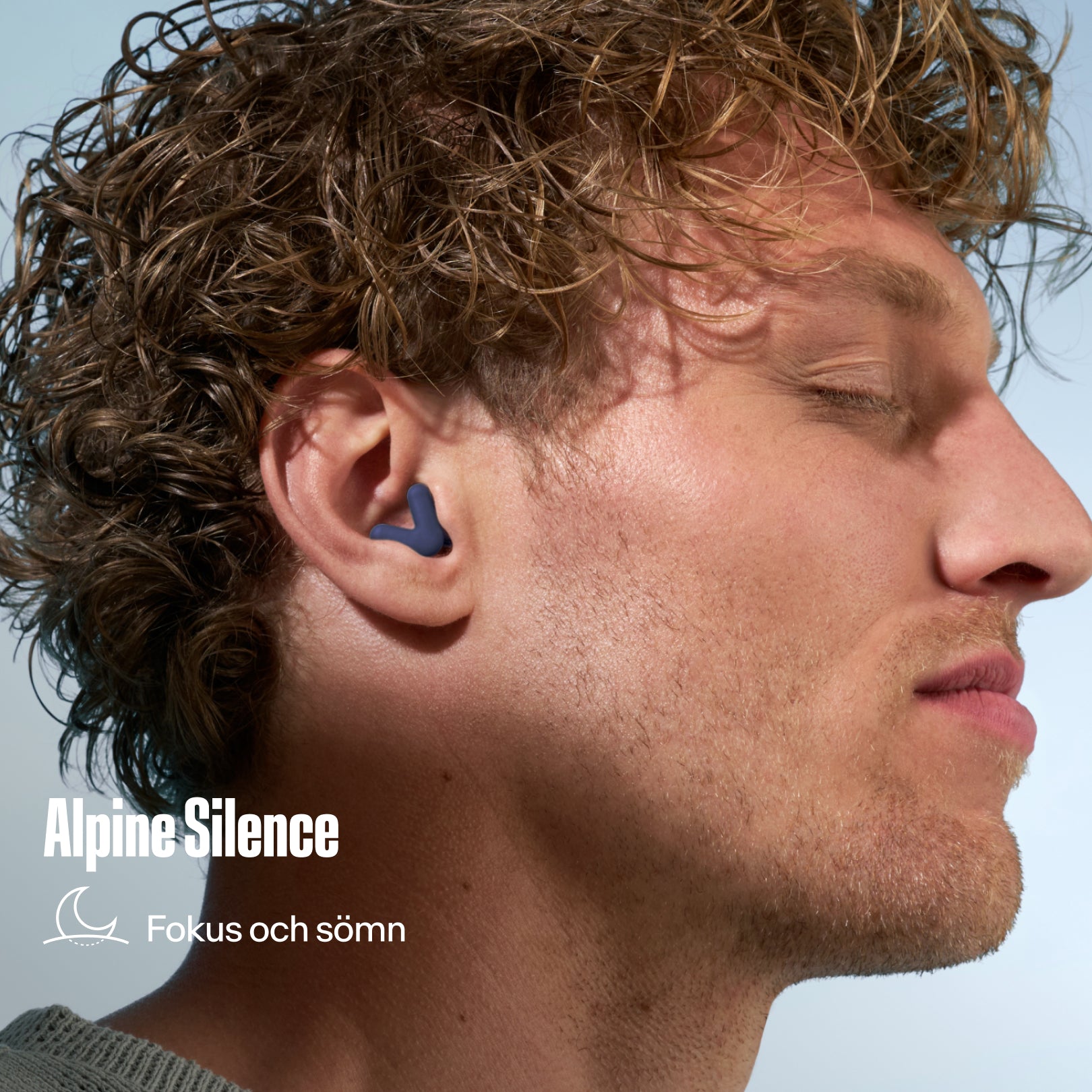 Alpine Silence öronpropp i örat på en man med lockigt hår, med texten &